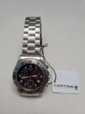 Certina automatic chronograph watch with a stainless steel link bracelet, silver-tone case, and a dark brown dial, shown with its white Certina brand tag on a light gray textured background.