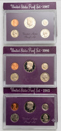 Three stacked sets of United States Proof Set coins from 1985, 1986, and 1987, each in a clear plastic holder with a purple backing card.